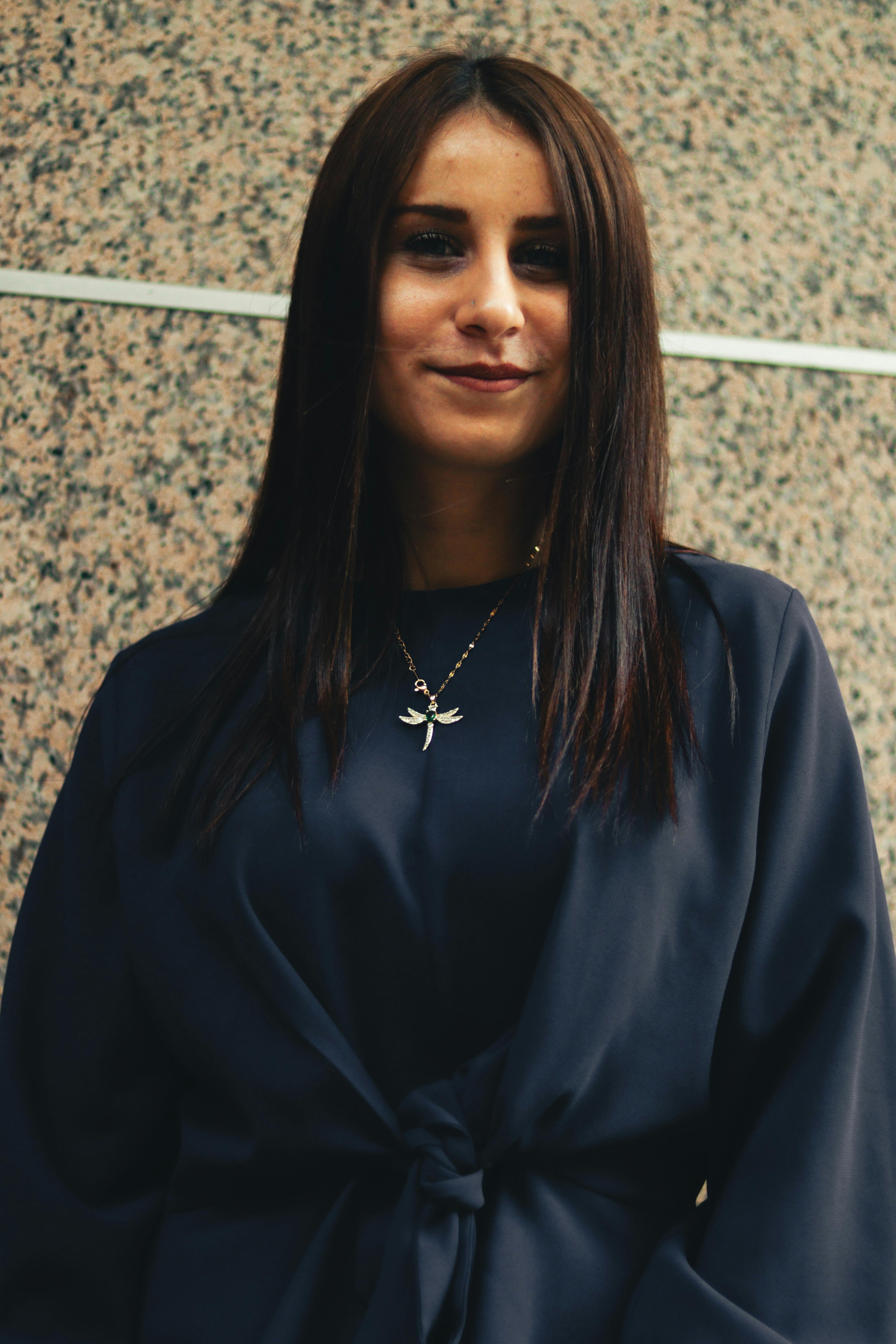 A smiling woman with long brown hair wearing dark clothes and a necklace.