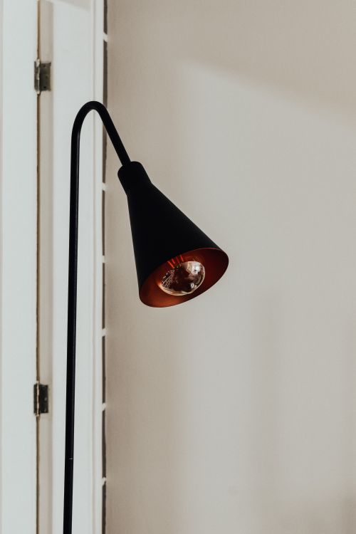 Free A minimalist black floor lamp casting soft light against a white door, perfect for modern interiors. Stock Photo