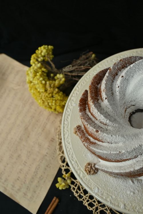 Free Top view of a Bundt cake dusted with powdered sugar, accompanied by yellow flowers, on a vintage platter. Stock Photo