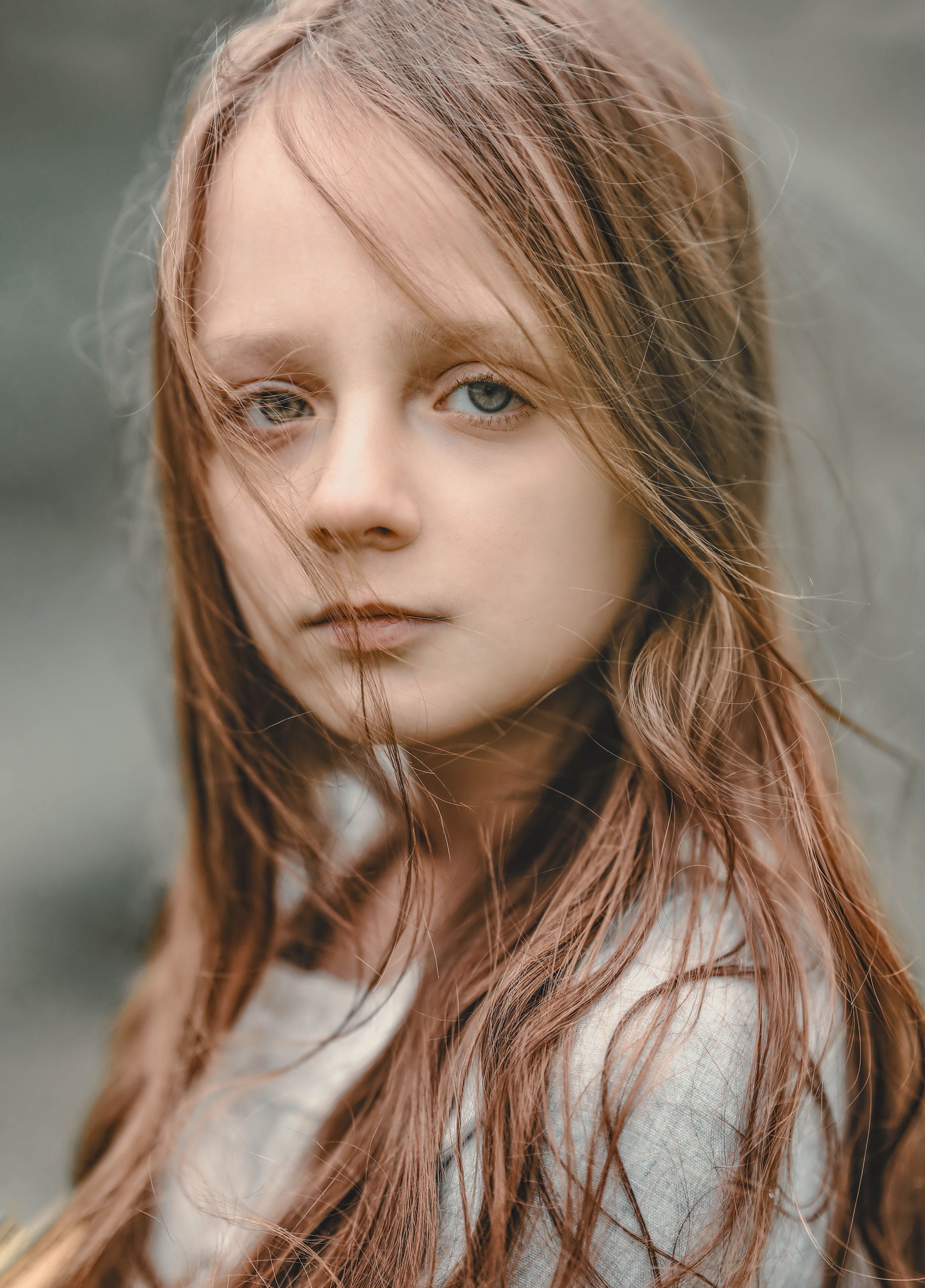Close-up portrait of a thoughtful girl with long brown hair in a natural outdoor setting.