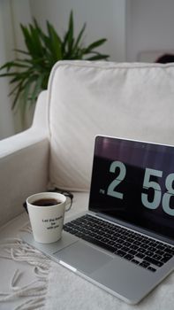 A laptop displaying a clock on a couch beside a coffee cup, creating a cozy workspace vibe.
