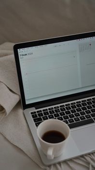 A cozy scene with a laptop displaying a calendar open next to a cup of coffee on a soft blanket.