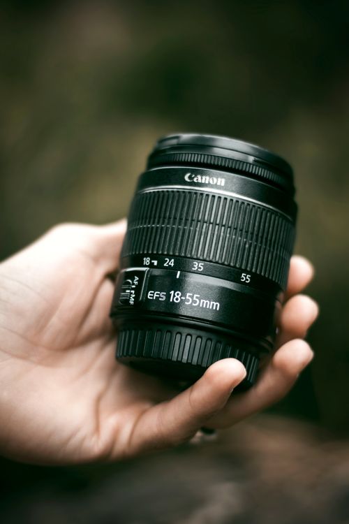 Free Vertical shot of a Canon DSLR lens held in a hand outdoors. Stock Photo
