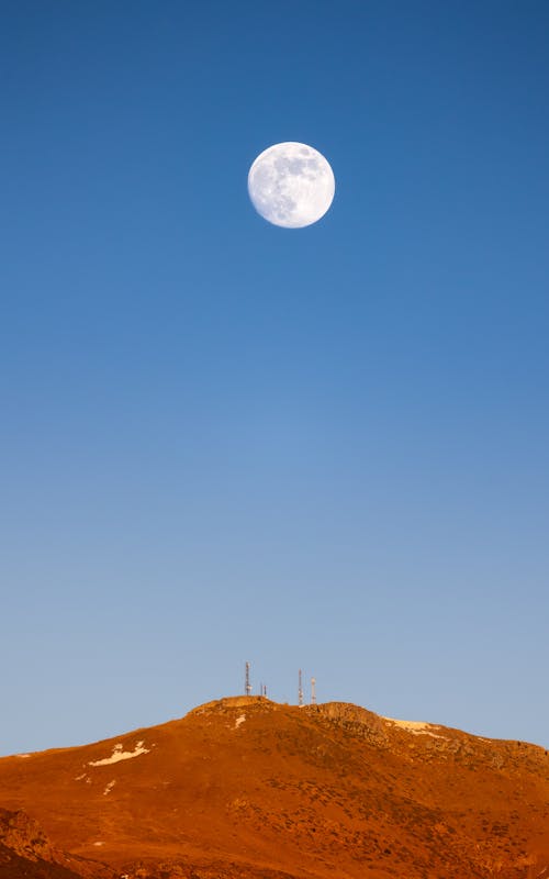 Free A full moon rising over a remote desert hill under a clear blue sky. Captivating night landscape. Stock Photo