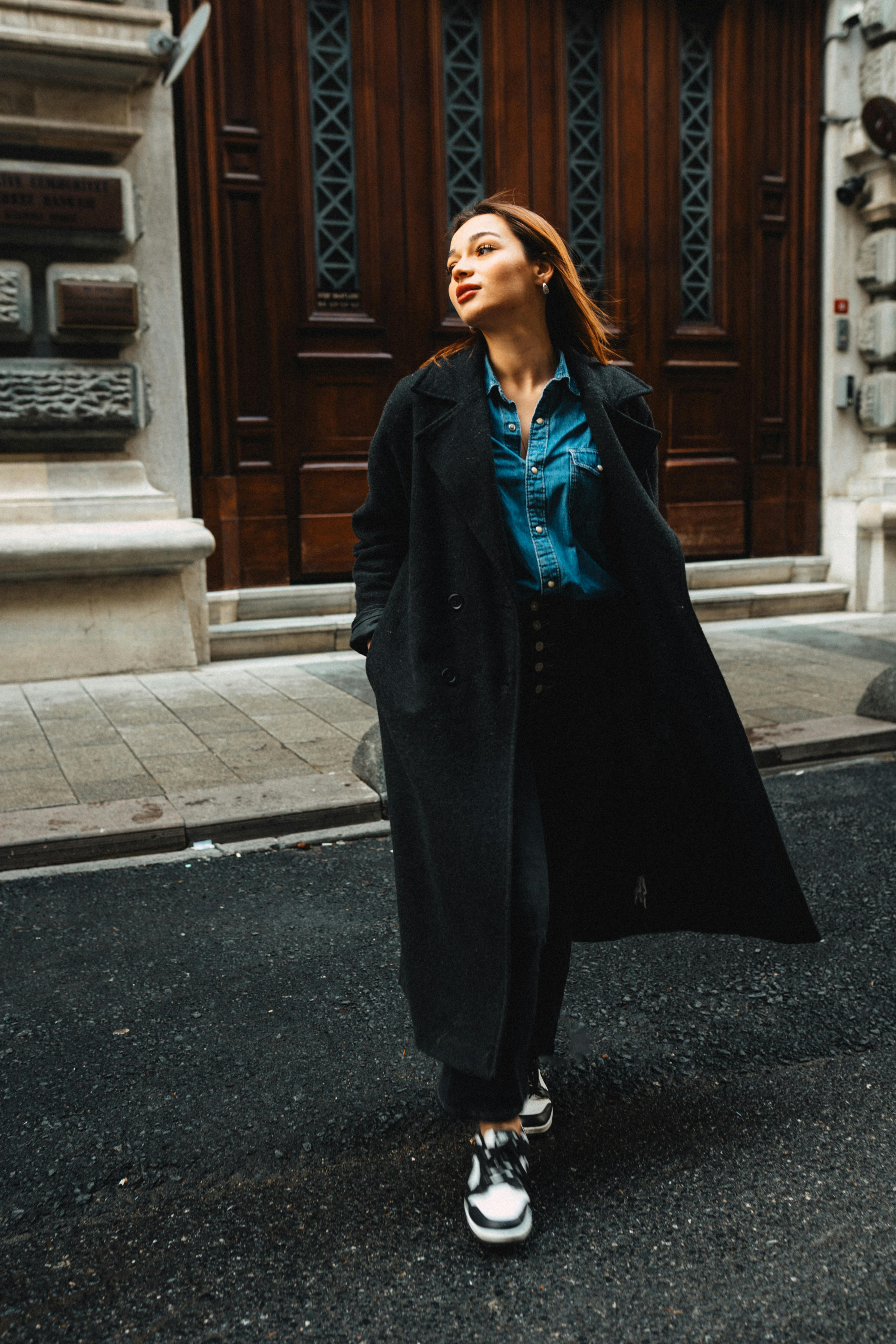 Stylish woman in a black coat walking on city streets with a confident expression.