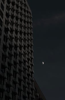 Low-angle view of a modern building against a dark night sky with the moon.