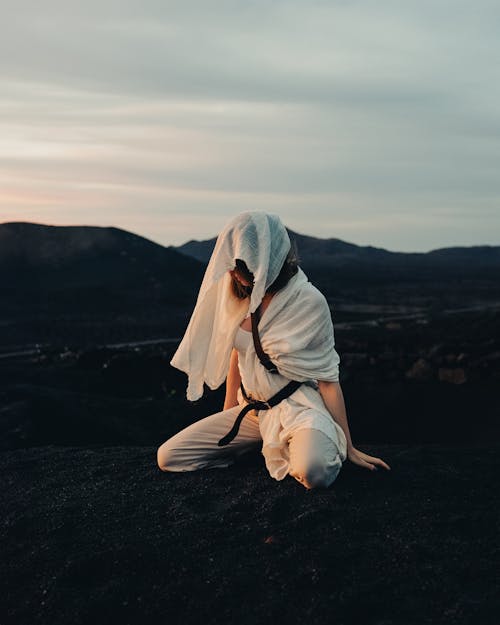 Woman in White Clothes and Veil Kneeling on Ground