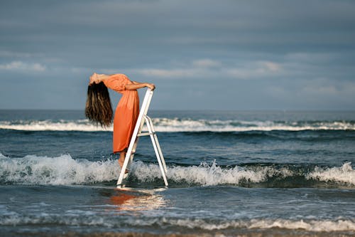 Woman in Dress Posing on Ladder on Sea Shore