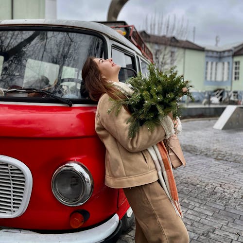 Woman Holding a Christmas Decoration and Leaning against a Vintage Bus