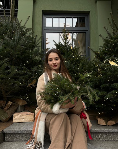 Smiling Woman Sitting with Christmas Trees and Evergreen Branches