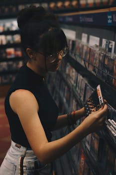 A young woman browsing CDs in a dimly lit music store, wearing eyeglasses and styled hair.