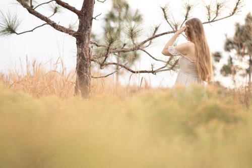 Free A woman with long hair stands in a rural setting wearing a dress, exuding serenity and connection to nature. Stock Photo
