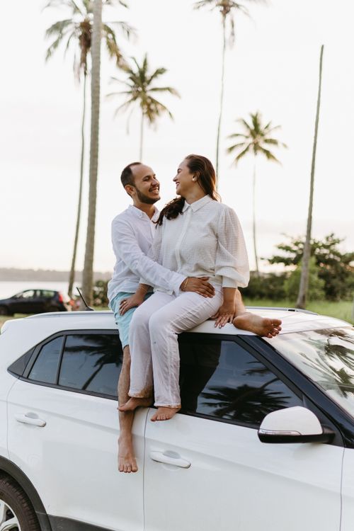 Free Happy couple enjoying a moment together on a car roof surrounded by palm trees, conveying love and joy. Stock Photo
