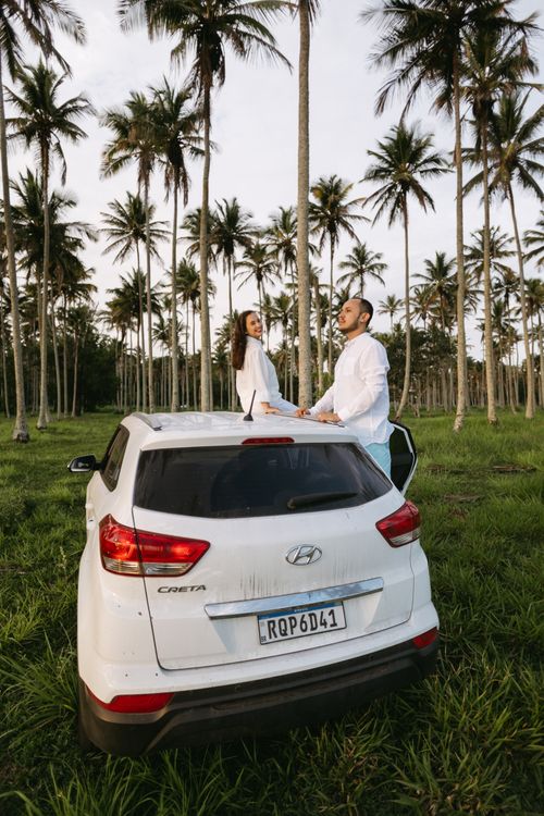 Free A couple in white shirts posing on a Hyundai Creta surrounded by tropical palm trees. Stock Photo