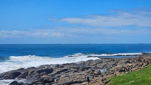 Free Scenic rocky shoreline with waves crashing under a bright blue sky, perfect nature scenery. Stock Photo