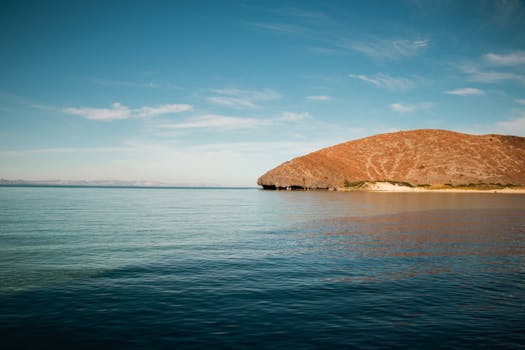 Tranquil image of a rocky coastal shoreline with clear blue water and an expansive sky.