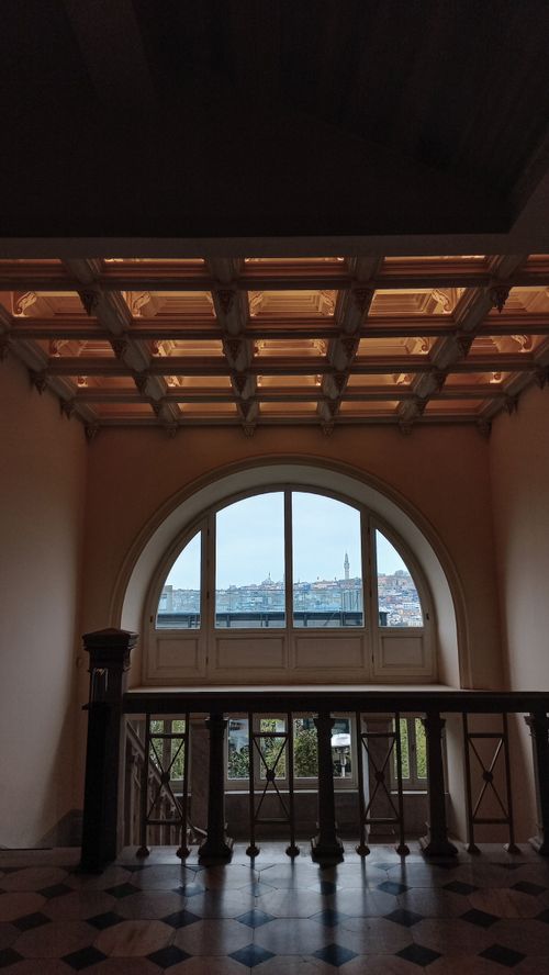 Free Elegant interior featuring an arched window with a cityscape view, framed by a wooden ceiling and intricate railing. Stock Photo