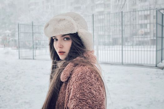 A young woman wearing winter clothes stands outdoors in a snowy urban setting.