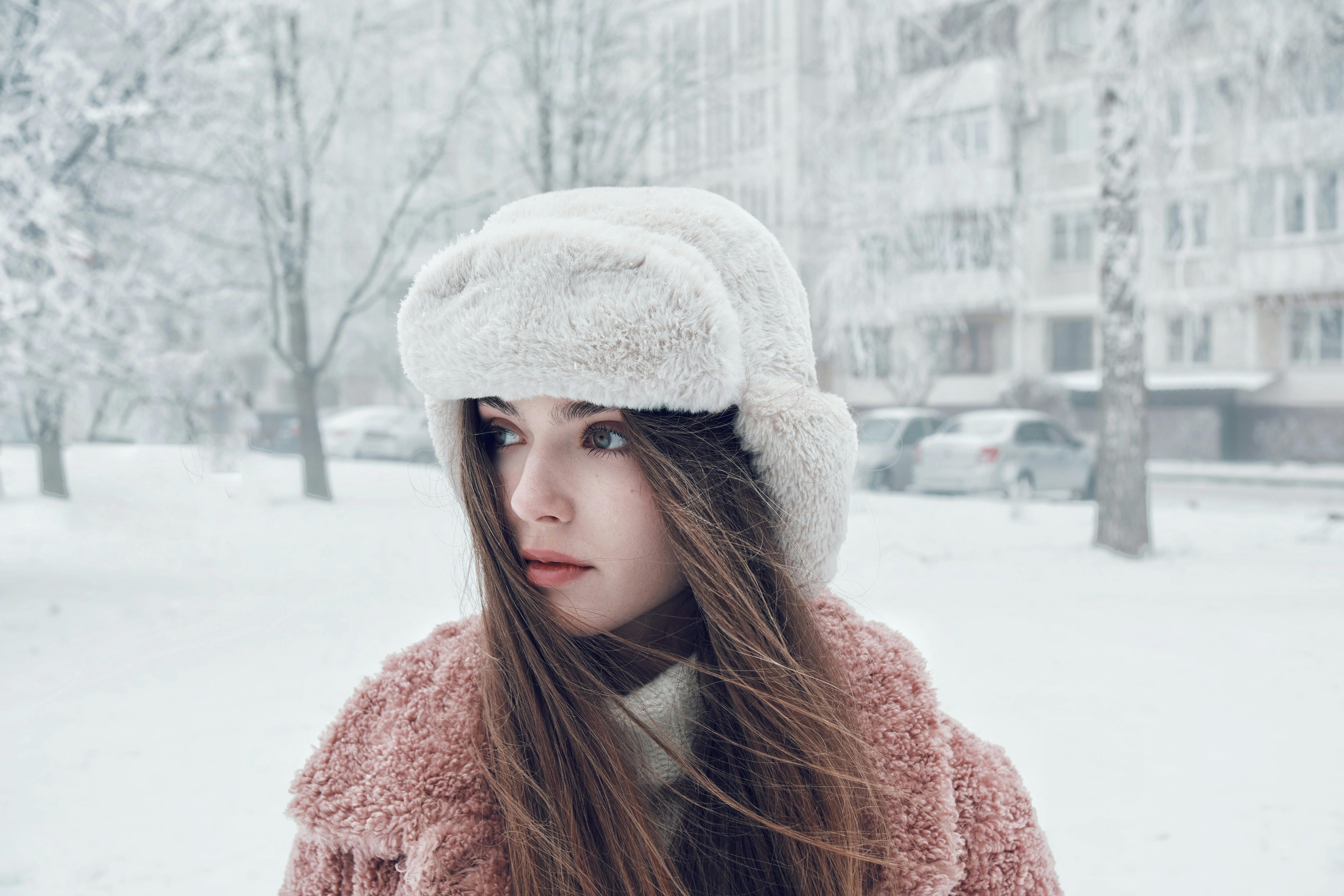 Stylish woman in winter attire with a furry hat, standing in a snowy urban setting.