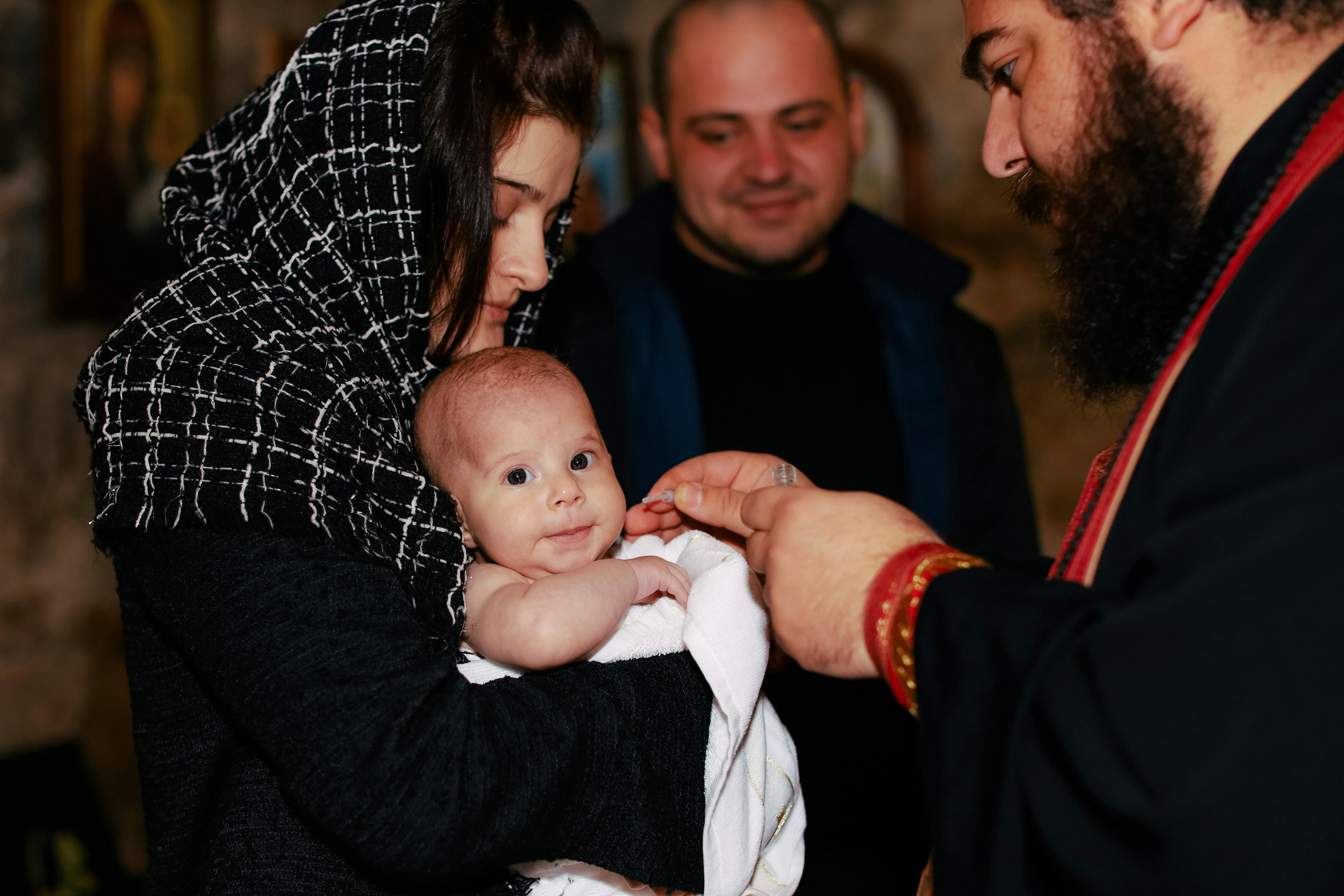 A traditional Orthodox baptism featuring a priest, baby, and family in an intimate ceremonial setting.
