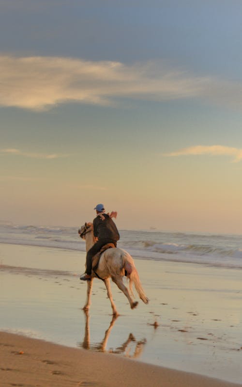 A Person Horseback Riding on a Beach at Sunset