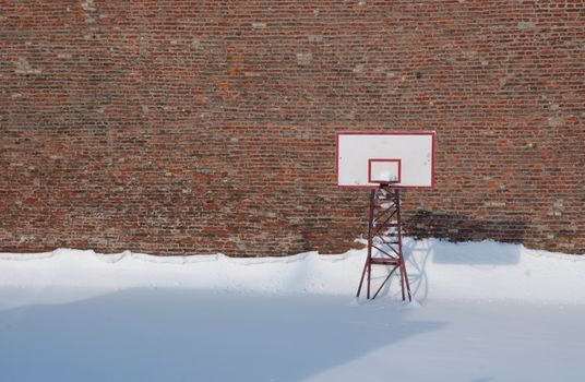 Snow-covered basketball court with hoop and red brick wall in Belgrade, Serbia.
