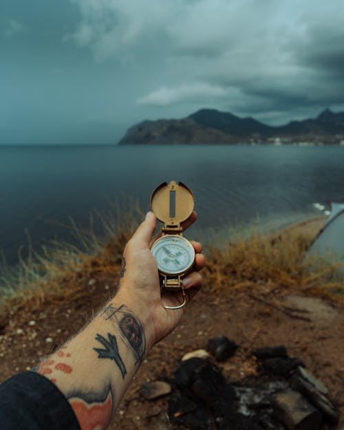 Man Hand with Tattoos Holding Compass on Sea Shore