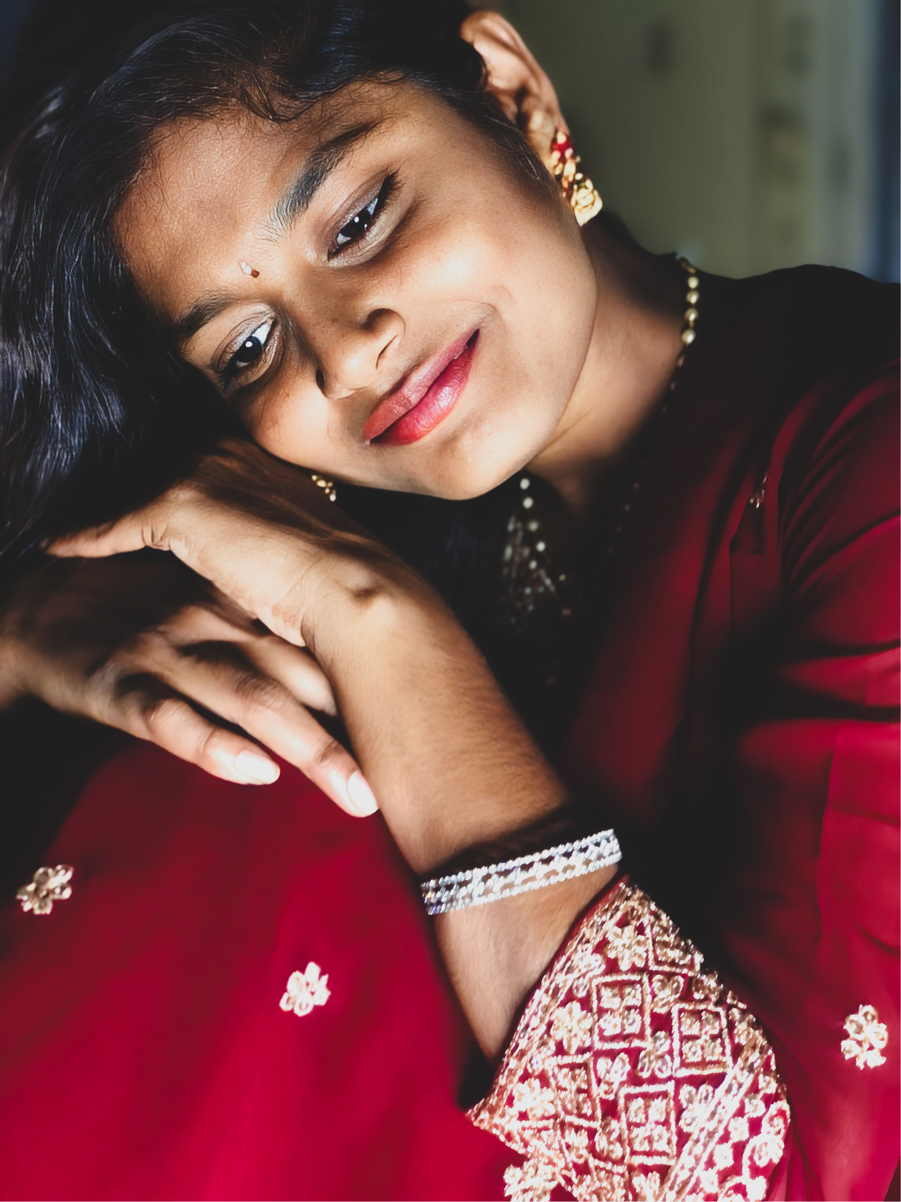 Portrait of a woman wearing traditional red clothing, resting her head thoughtfully on her arms.