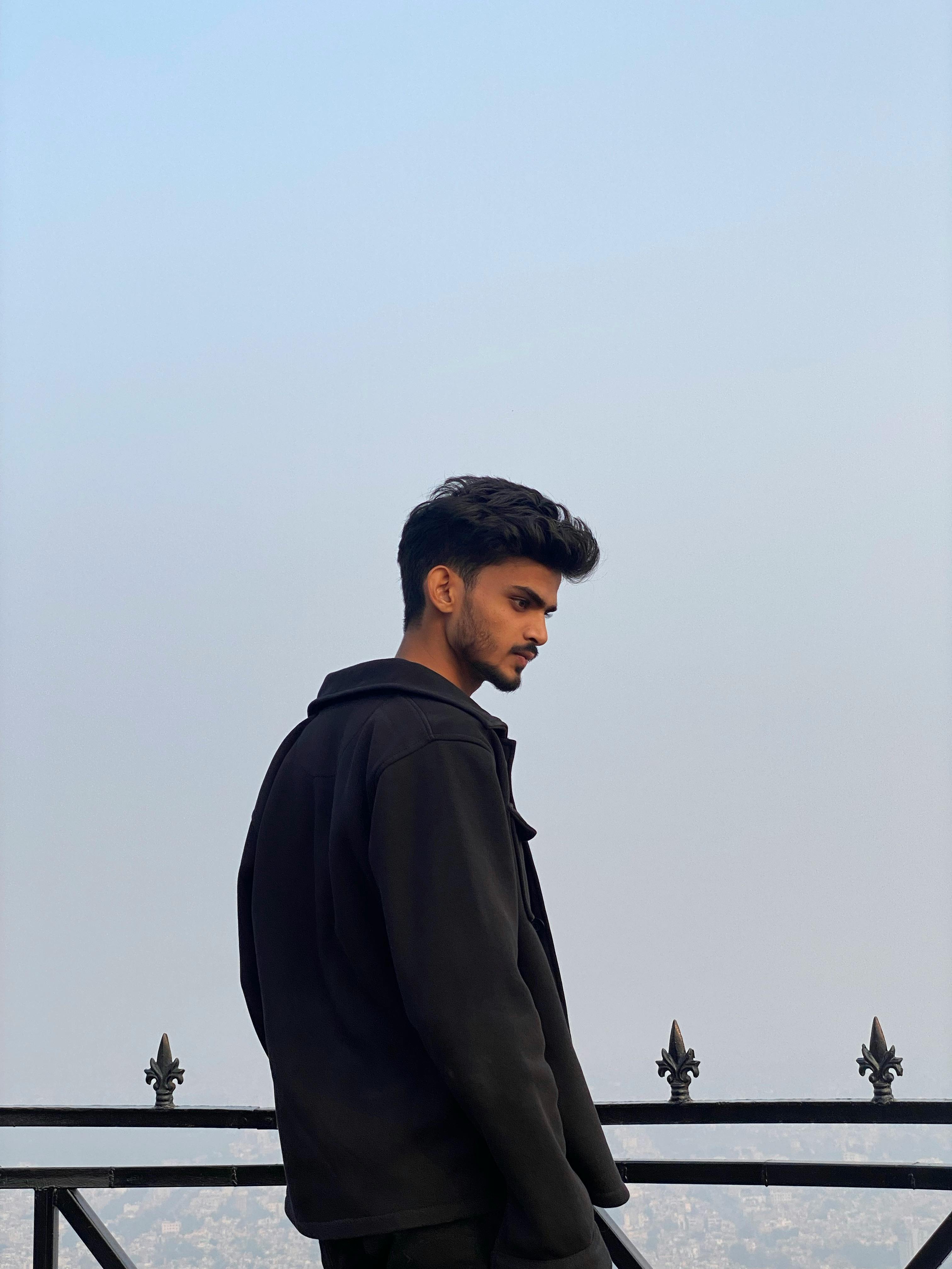 Side profile of a young man in a black jacket posing against the sky in Alwar, India.