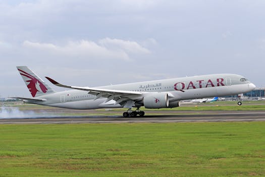 Qatar Airways airplane touches down on runway with smoke, clear sky, and green grass.