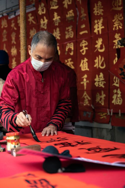Free A calligrapher in a red robe writes with ink during a cultural event indoors. Stock Photo