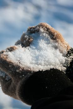 Close-up of hands wearing gloves holding snow in bright winter sunlight.