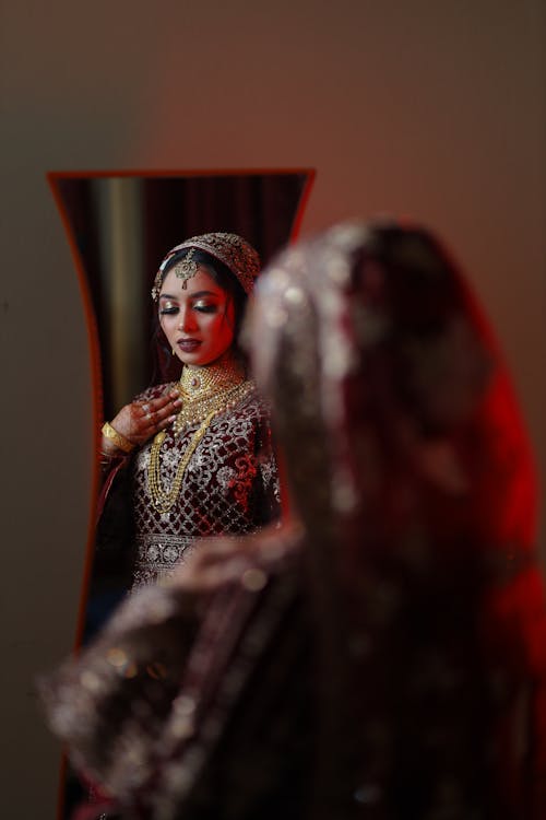 Bride Wearing a Traditional Dress and Jewelry Standing in Front of a Mirror 