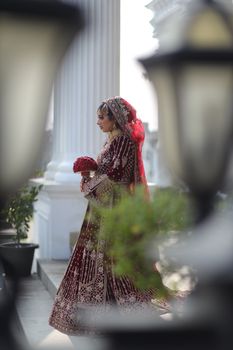 Beautiful bride in traditional attire with intricate embroidery holding bouquet outdoors.