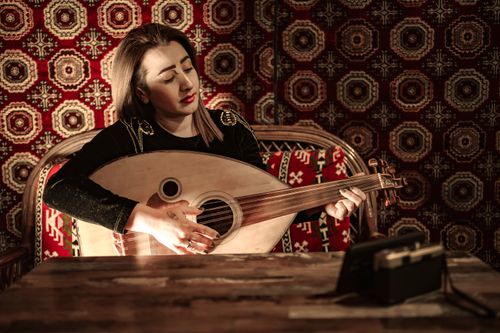 Free A young woman plays the oud in a traditional Turkish setting, surrounded by rich patterns and warm lighting. Stock Photo