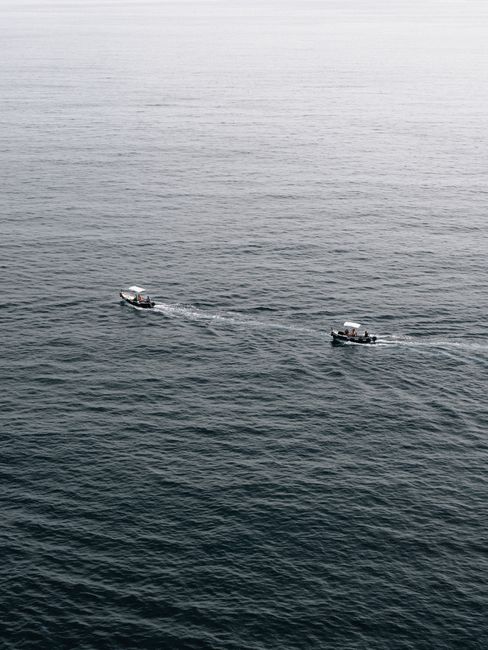 Aerial view of two boats sailing on a calm sea, creating subtle waves.