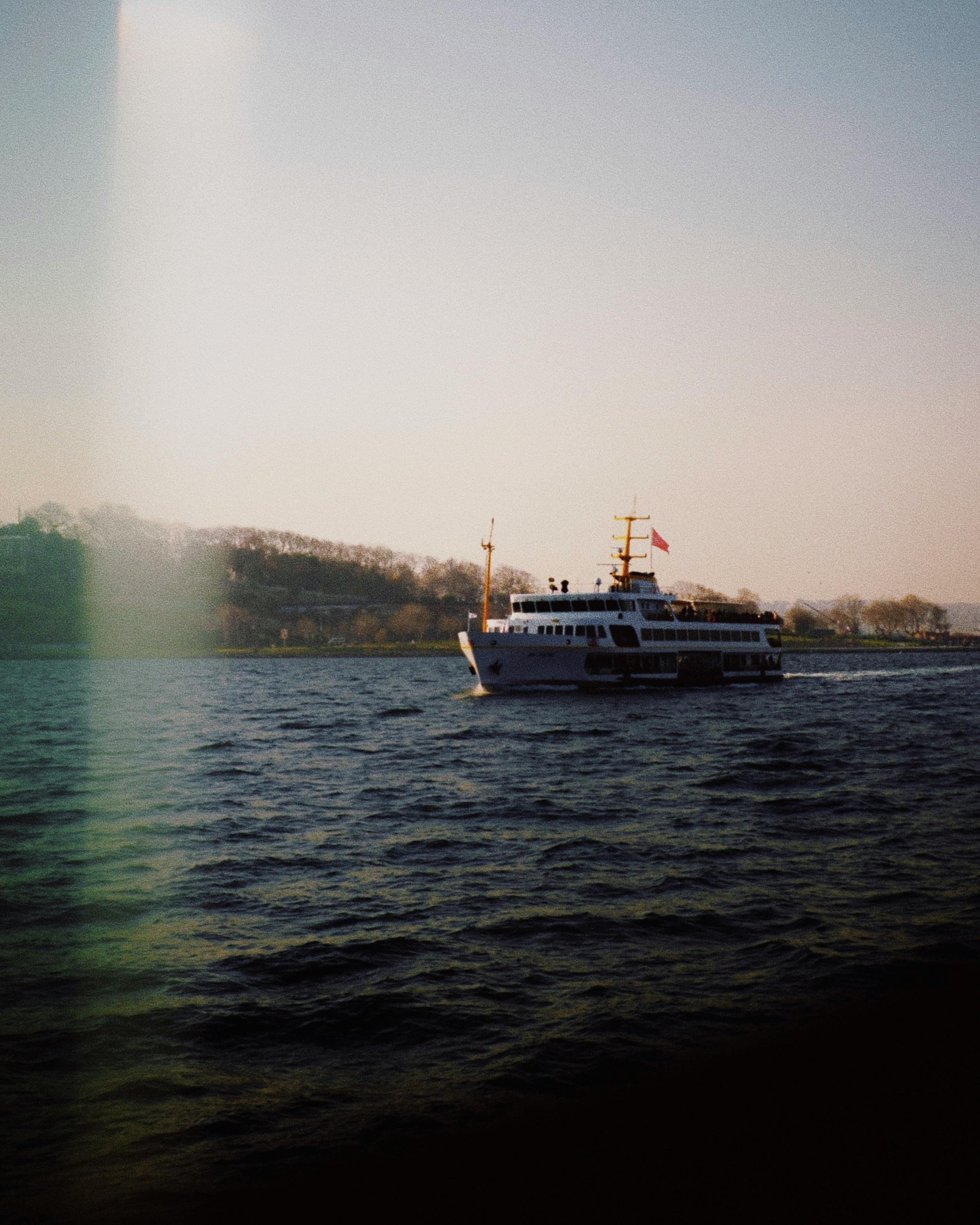 A passenger ferry cruising on tranquil sea against a scenic coastal backdrop during sunset.
