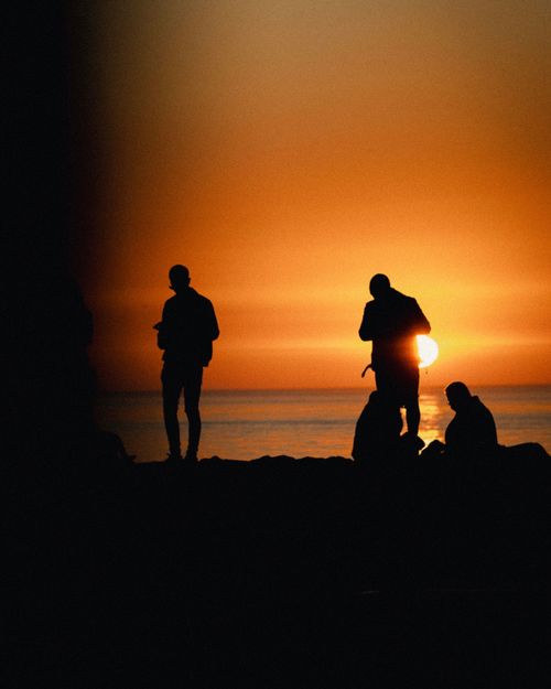 Free A group of friends silhouetted against a vibrant sunset on a beach, capturing a serene moment. Stock Photo
