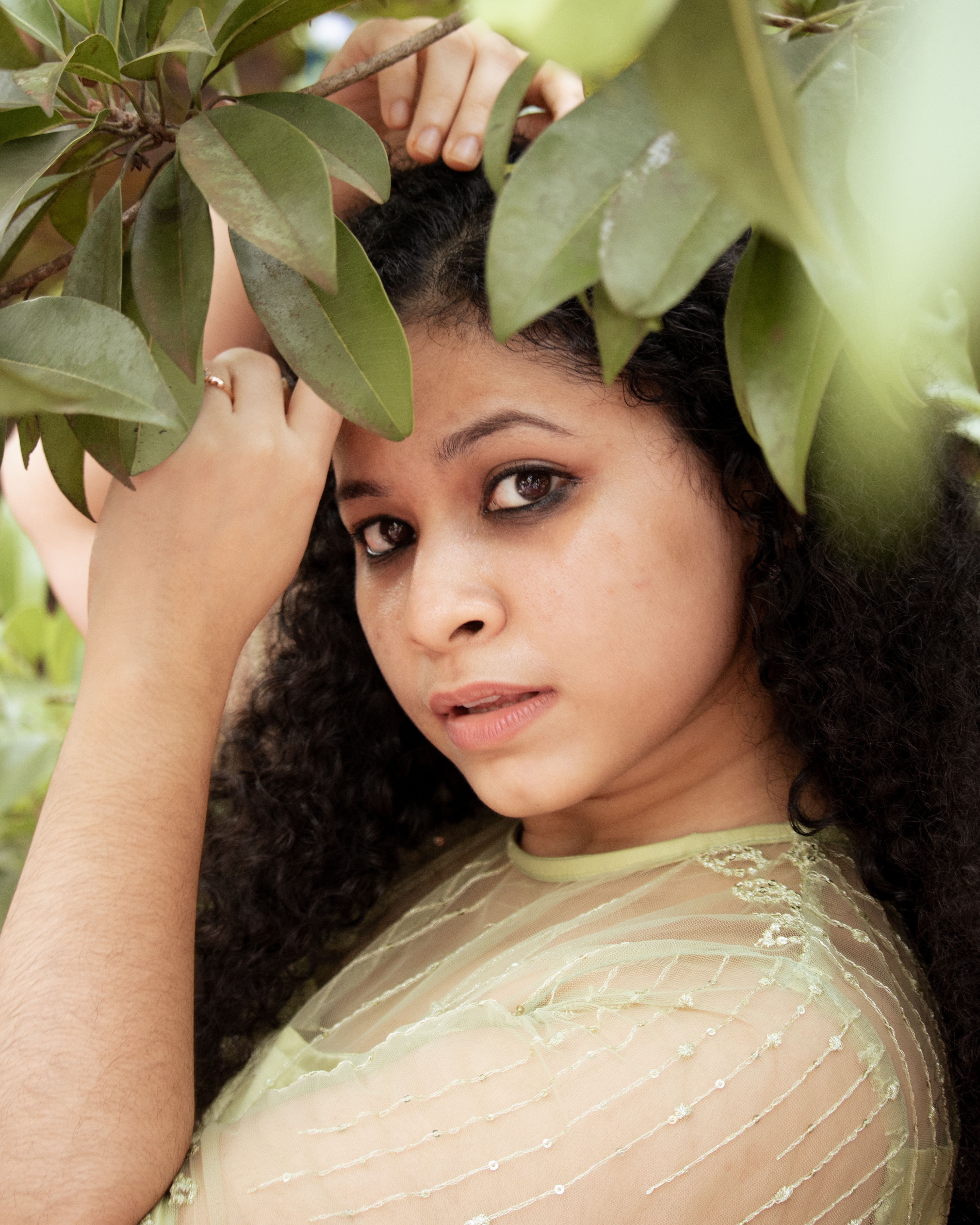 A captivating portrait of a woman in a green dress surrounded by lush leaves, conveying a connection with nature.