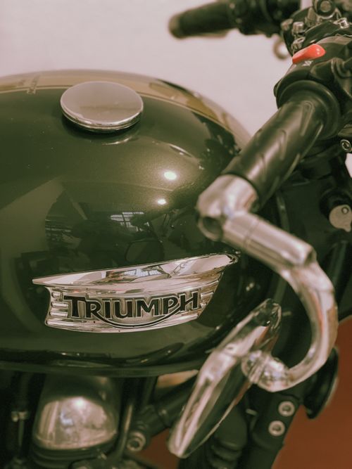 Free Detailed view of a green Triumph motorcycle fuel tank showcasing the iconic logo and retro styling. Stock Photo