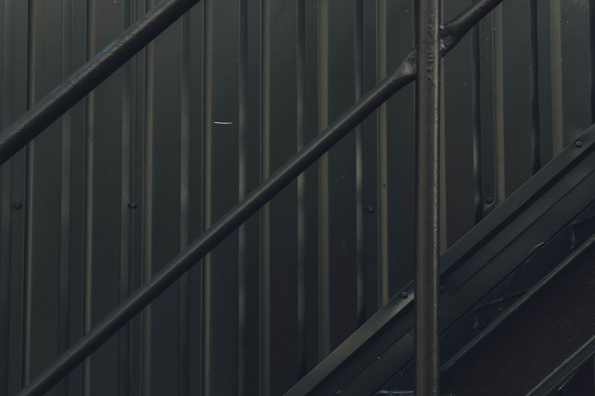 Scară industrială cu balustradă metalică din montanți verticali, în fața unui perete din tablă ondulată