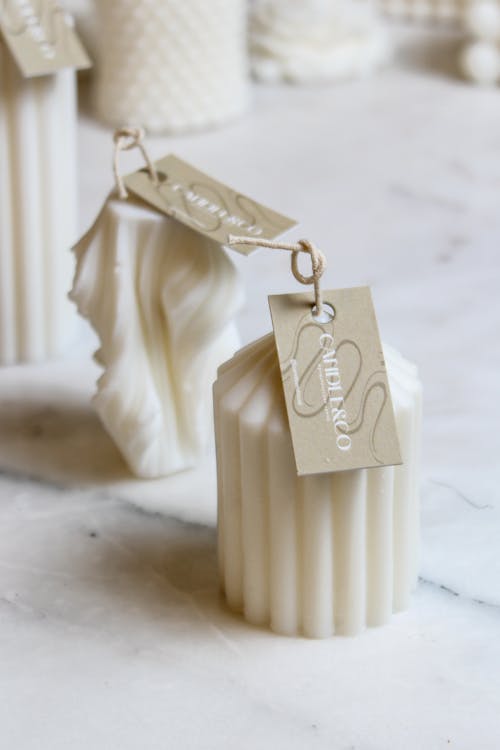 Free Minimalist white candles with tags on a marble surface, perfect for decor. Stock Photo