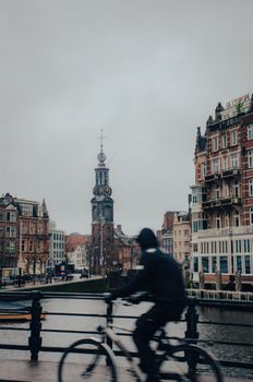 Blurred cyclist crossing a canal bridge in Amsterdam with iconic city architecture in the background.