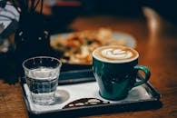 室内的托盘上放着一个充满活力的绿色马克杯，杯子上有卡布奇诺拉花和饼干