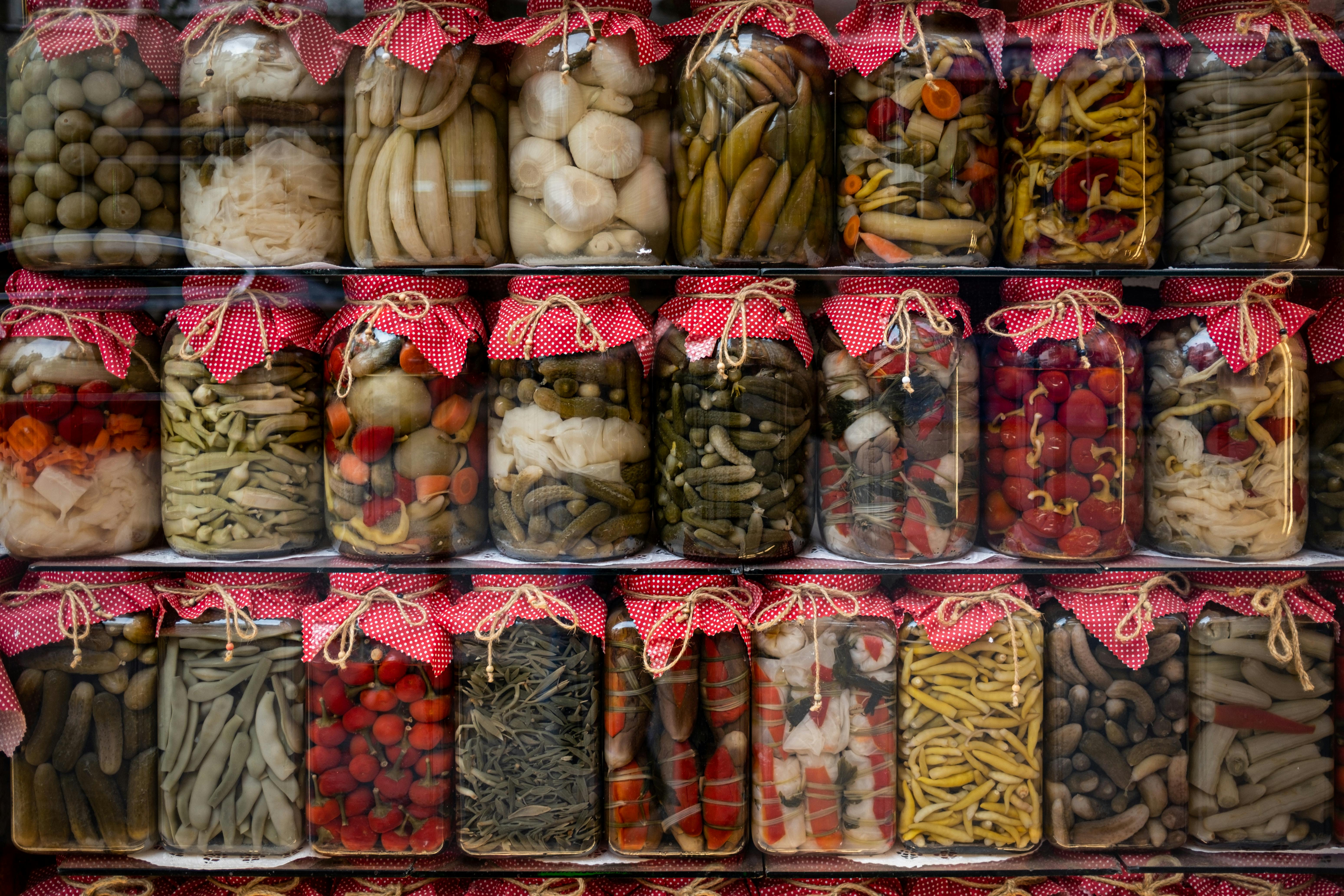 Vibrant assortment of pickled vegetables in jars with red fabric covers, displayed on shelves.