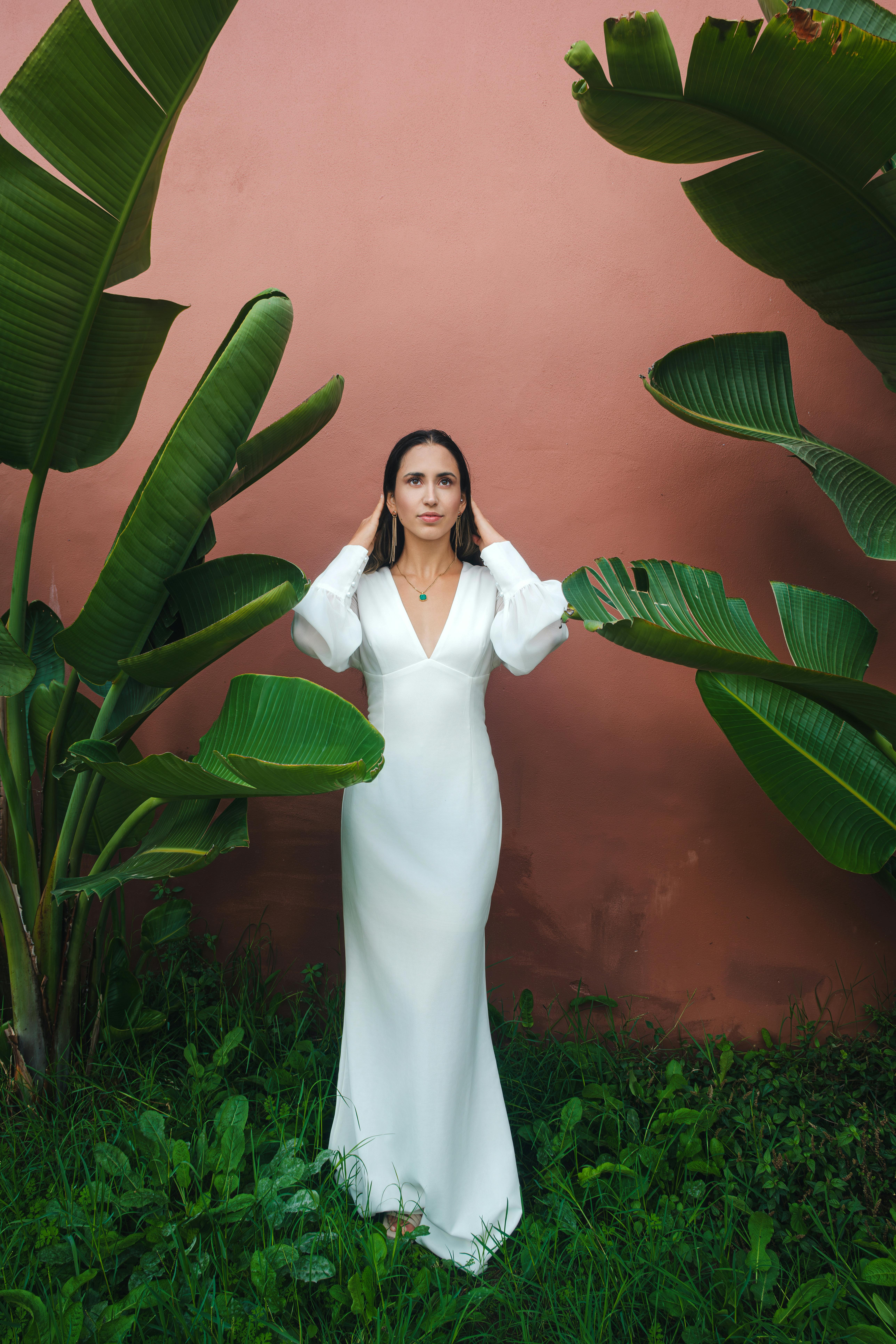 A bride poses elegantly among lush tropical plants in Lisbon. Ideal for wedding themes.