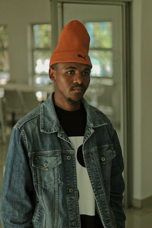 Young Man in a Denim Jacket and a Hat Standing in a Room 