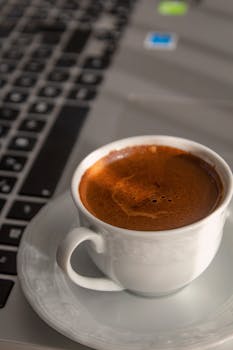 A cup of freshly brewed coffee overlooks a laptop keyboard, perfect for productivity.