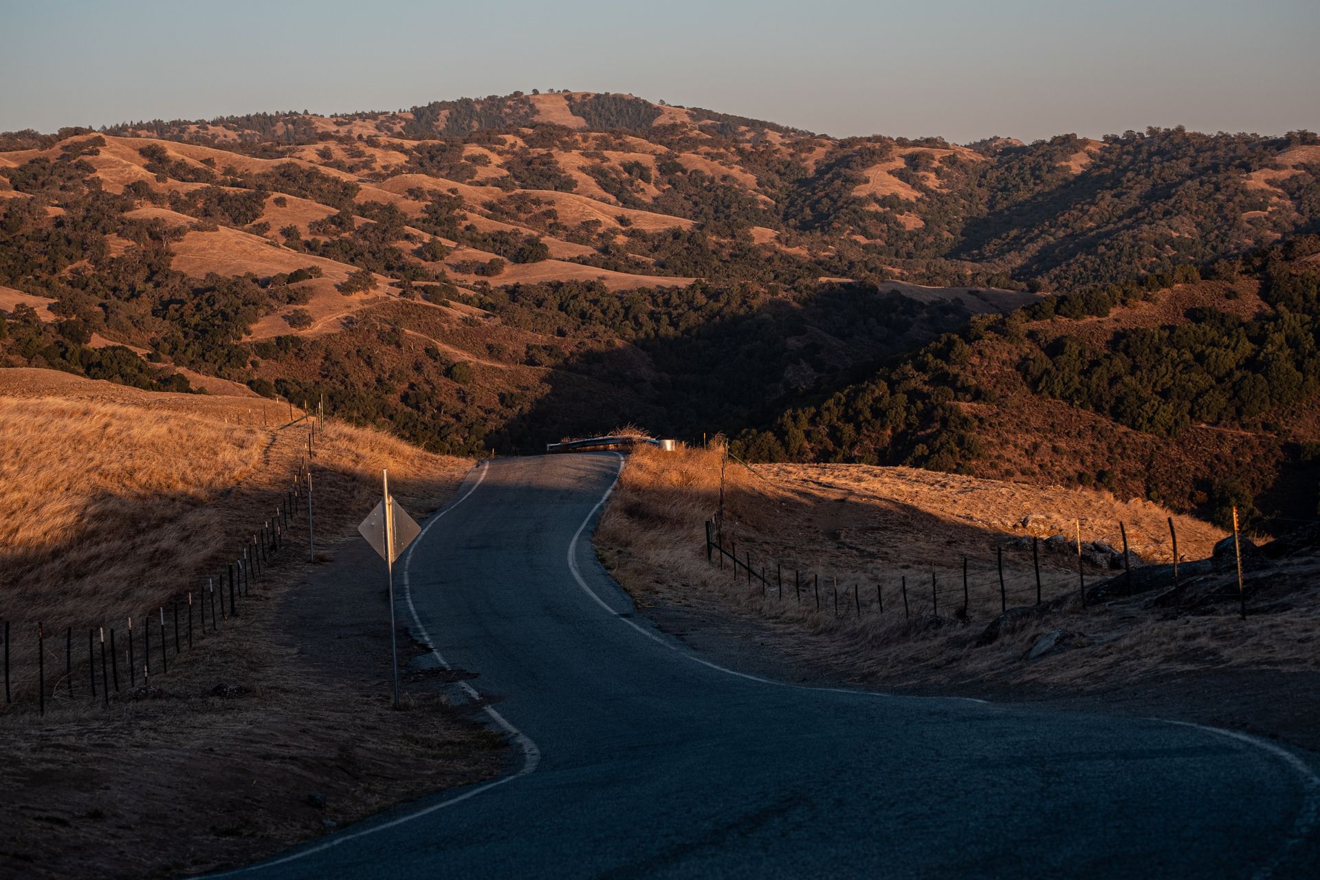A road curving through open hills at last light — Mo Eid on Pexels