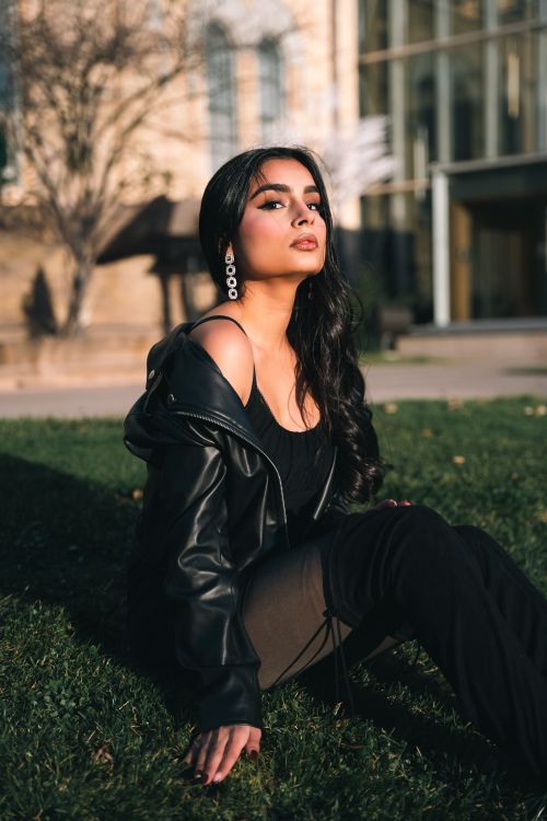 Free Fashionable woman sitting on grass in a black leather jacket and boots. Stock Photo